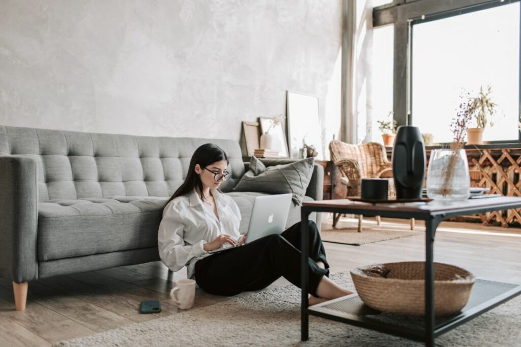 Woman sitting on the floor in her living room working on her laptop.